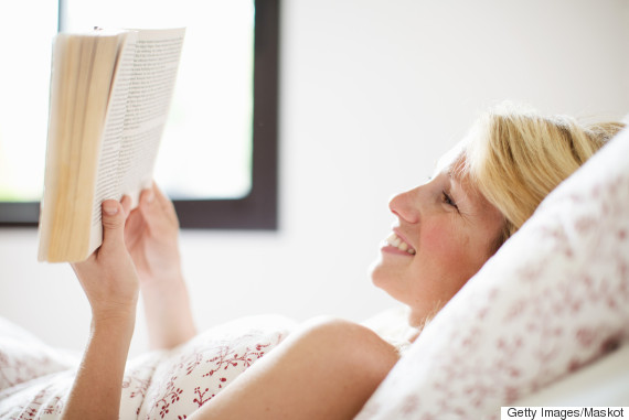Happy mid adult woman lying on bed and reading book